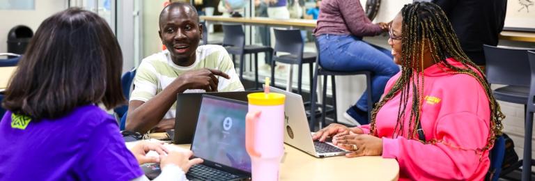 A group of diverse international students sit chatting and laughing at a table in RDP's Global Hub
