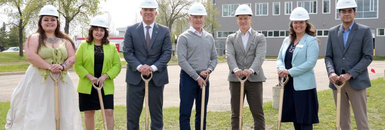 A group of RDP and Government of Alberta reps wear hardhats while holding shovels