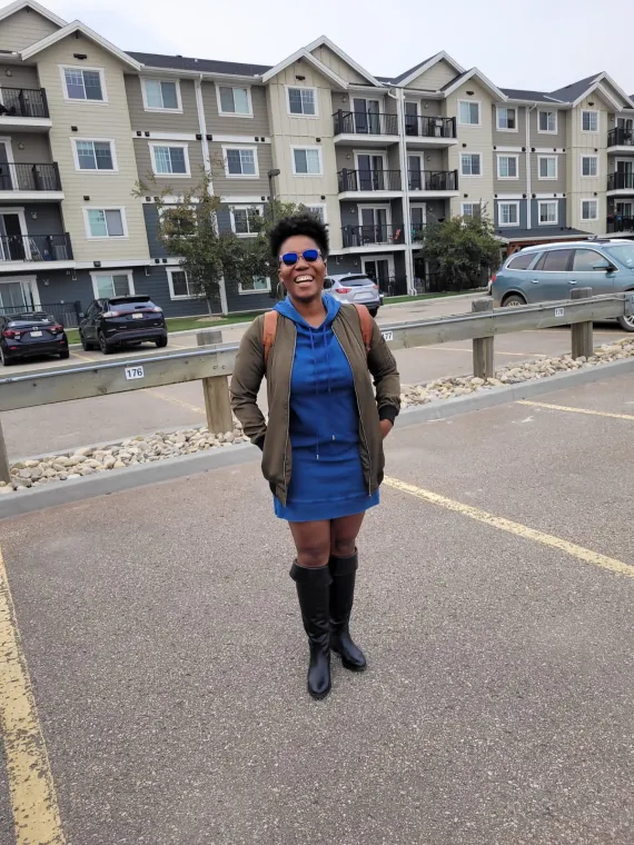 Nikeisha Sewell Lewis smiles in a parking lot wearing a blue dress and sunglasses