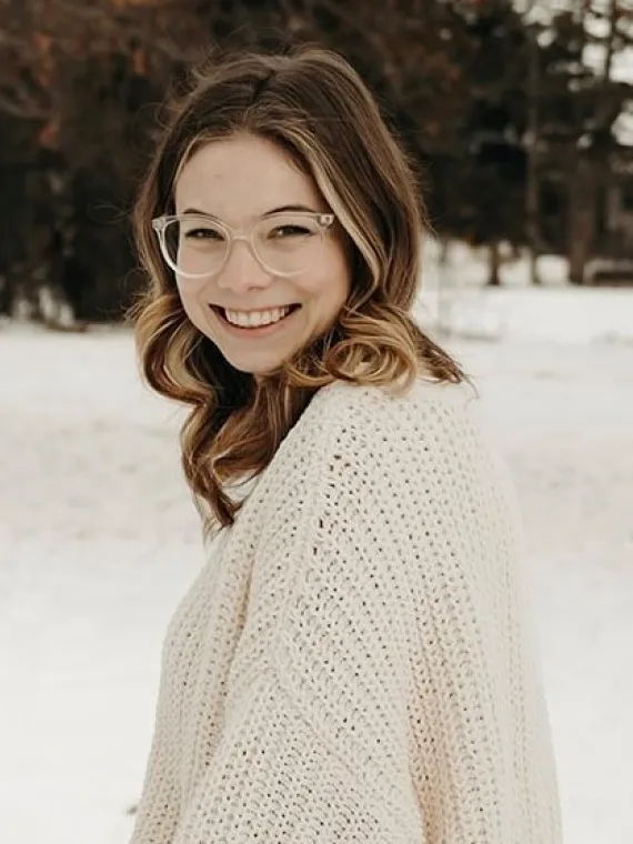 Aubrey Reed turns to smile at the camera wearing a white sweater against a snowy background
