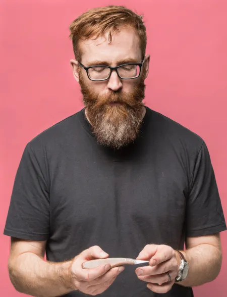 Robin, in a grey tshirt standing against a pink background, looks down at a cutting tool in his hands.