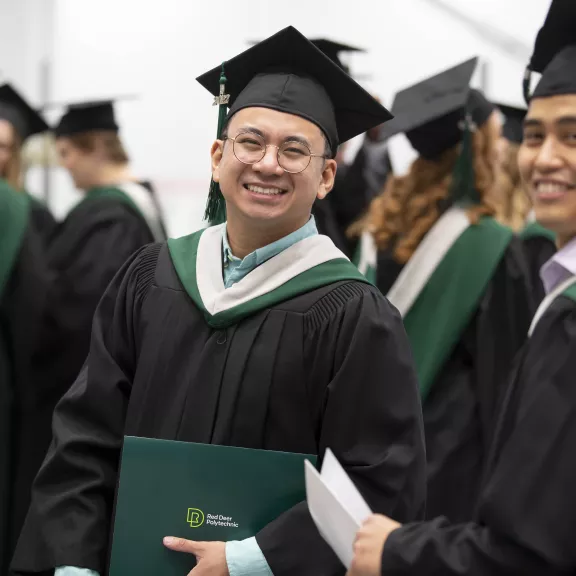 Students at convocation smiling in their cap and gowns 