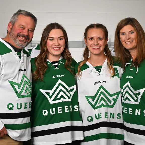 Smiling picture of a family of 4 wearing Queens hockey jerseys