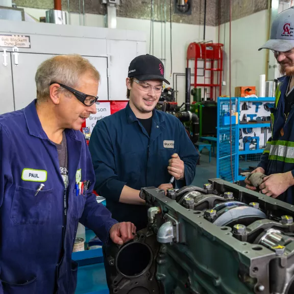 An instructor looks at the engine two students are working on.