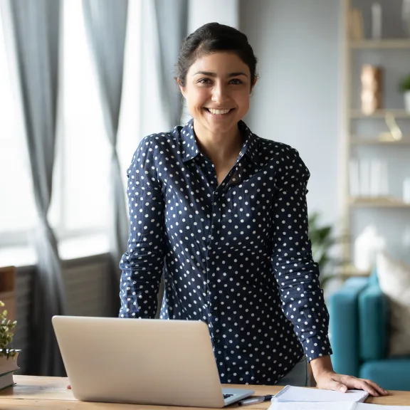 Young woman standing at desk looking at the camera.