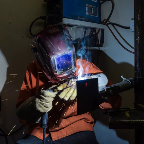 A student welding in a lab wearing protective equipment including helmet.