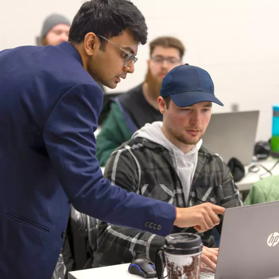A male faculty member points at a student's laptop while his student looks at the screen