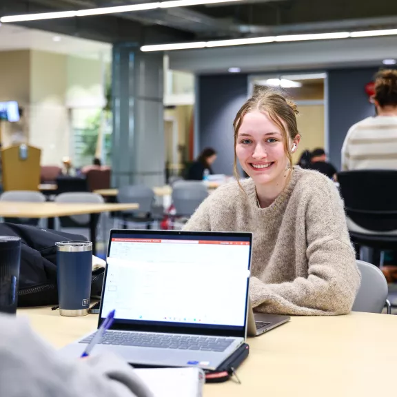 Students studying in the library. One student smiles at the camera.