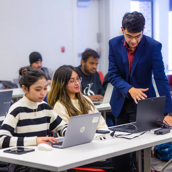 An instructor showing student something a laptop. The student beside them works on their laptop.