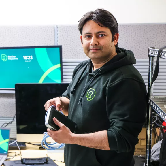 A network administrator working on computer parts, slightly smiles at the camera.