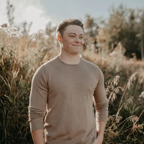 A smiling Colton Campbell stands against a field of long grass