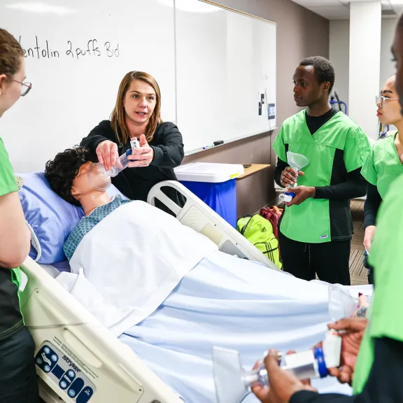 An instructor shows students how to properly apply an inhaler mask on a mannequin's face.