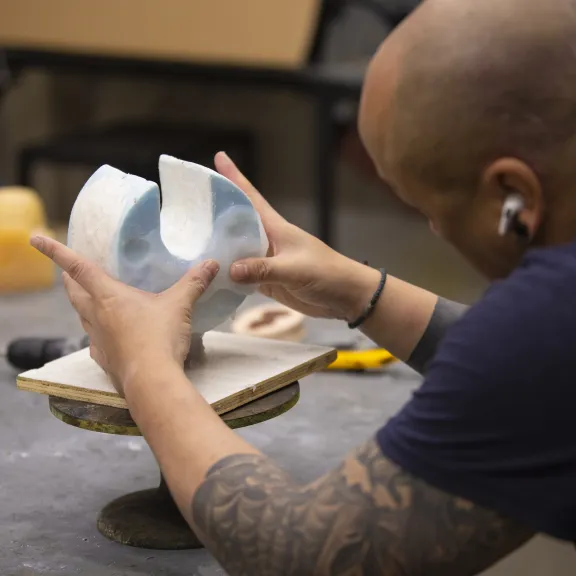 An artist works on a crescent shaped sculpture.