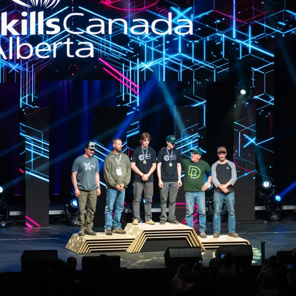 A group of students and staff stand on a podium with their medals at the SkillsCanada Alberta Games