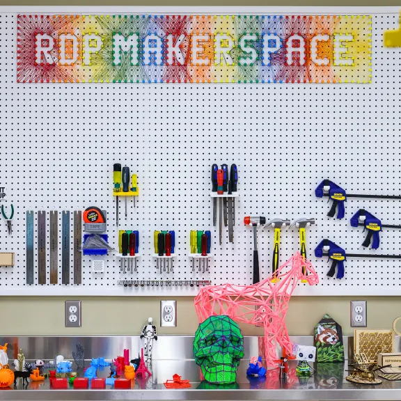 The makerspace wall features a peg board with tools hung along the bottom and a metal shelf with sample projects.