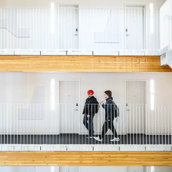 A wide shot of two male students walking in RDP's new residence. You can see multiple floors made of clean white walls and bright coloured wood. 