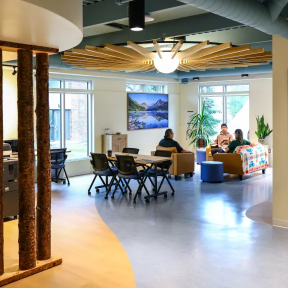 Three people sit on chairs and couches in the Pónokaisissáhta Indigenous Student Centre