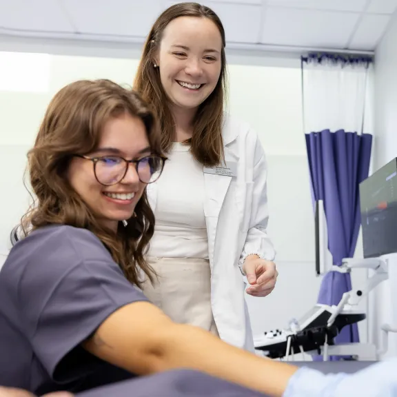 An instructor supervises two students practicing artery ultrasounds.