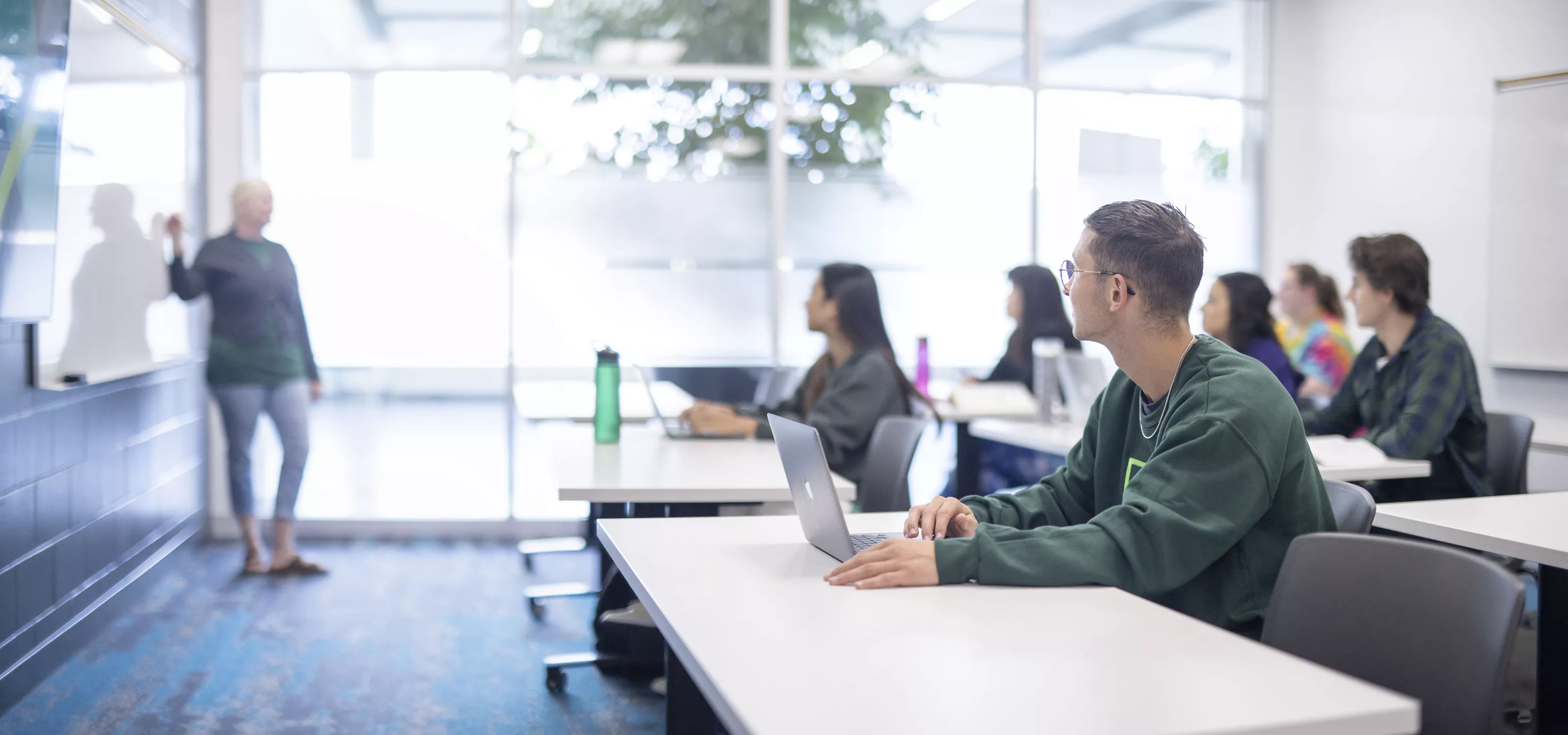 Students with laptops looking at instructor.