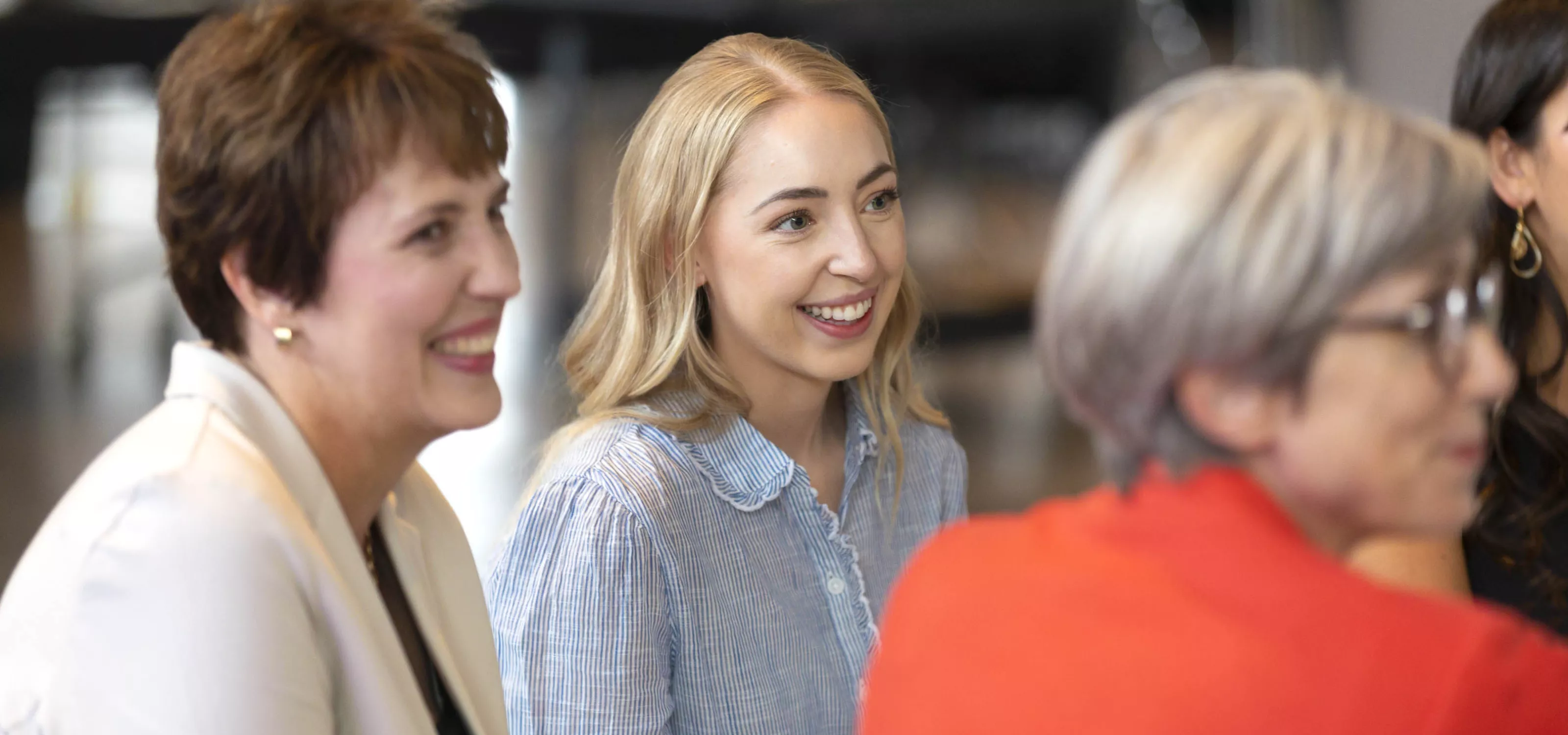 Women sitting at a table looking away from the camera and at each other.