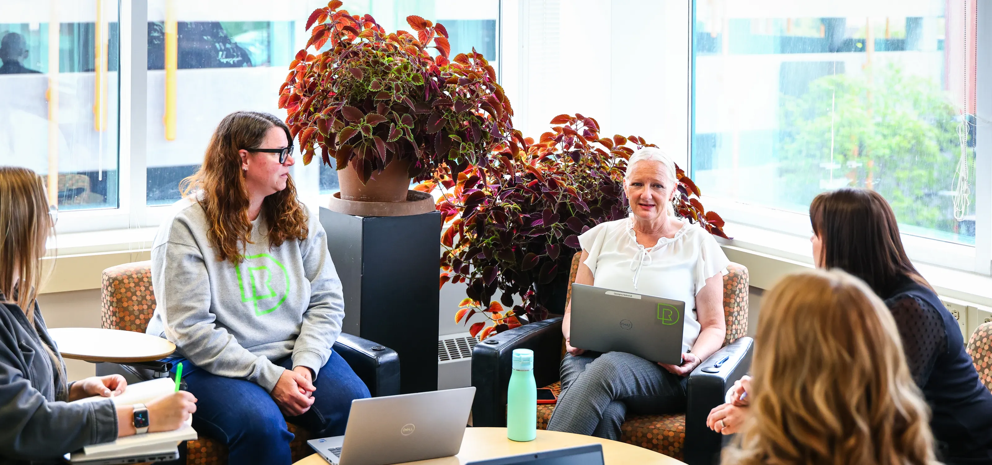 A circle of five people sitting down and talking in an open office.