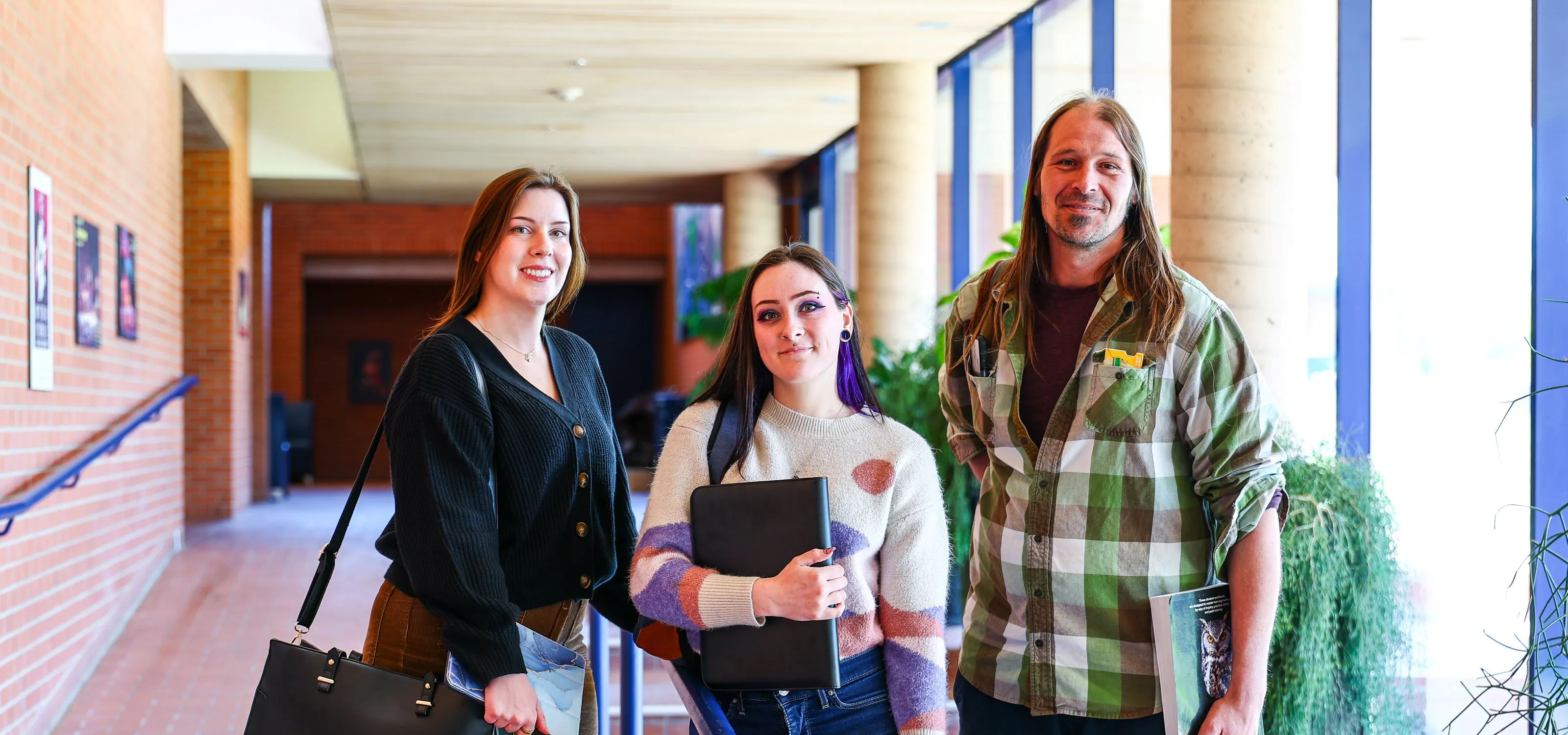 Two female and one male student stand with their books in the lobby of the Arts Centre at RDP